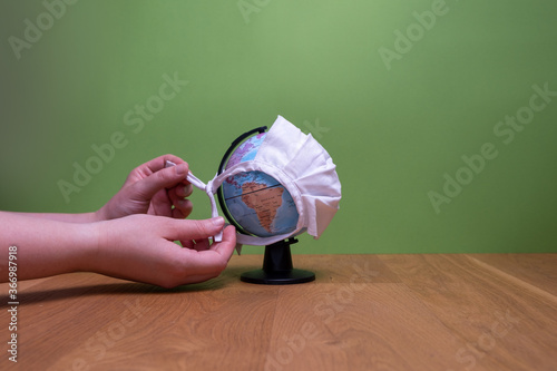 Frau bindet weiße Maske um Weltkugel auf Holztisch mit grünem Hintergrund mit Blick auf Amerika photo