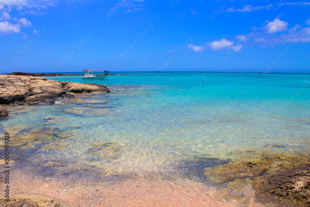 Beach with pink sand, stones and turquoise water and clouds in blue sky.