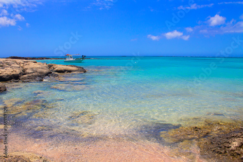 Beach with pink sand, stones and turquoise water and clouds in blue sky.