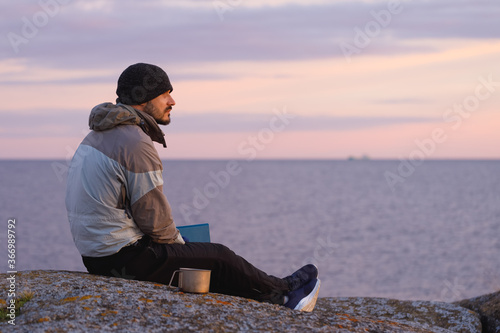 A man with a book on the background of the sea. The background is blurred.
