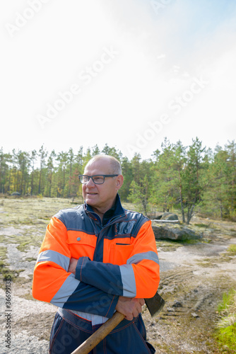 Portrait of happy mature handsome man thinking and holding ax in the forest