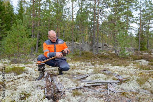 Portrait of mature handsome man sharpening ax in the forest