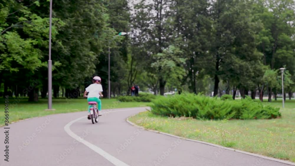 Cute little girl starts riding bicycle at park. girl in a protective helmet. Safety of children's activities concept. Cute little girl starts riding bicycle at park. girl in a protective helmet. Safety of children's activities concept.