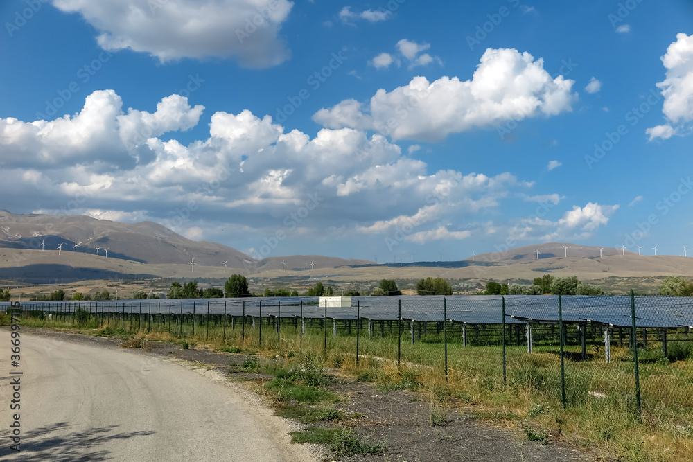 Power generation plant, with several solar panels and wind turbines in the background, commune of Pescina, Abruzzo region, province of Aquila, Italy