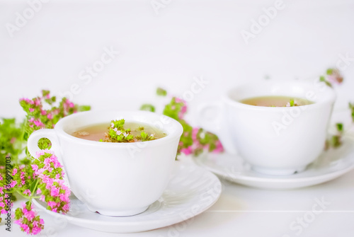 two cups of tea with oregano flowers on a white background close-up. cups of herbal tea and fresh flowers of oregano macro. background with herbal tea in cups and fragrant oregano flowers.