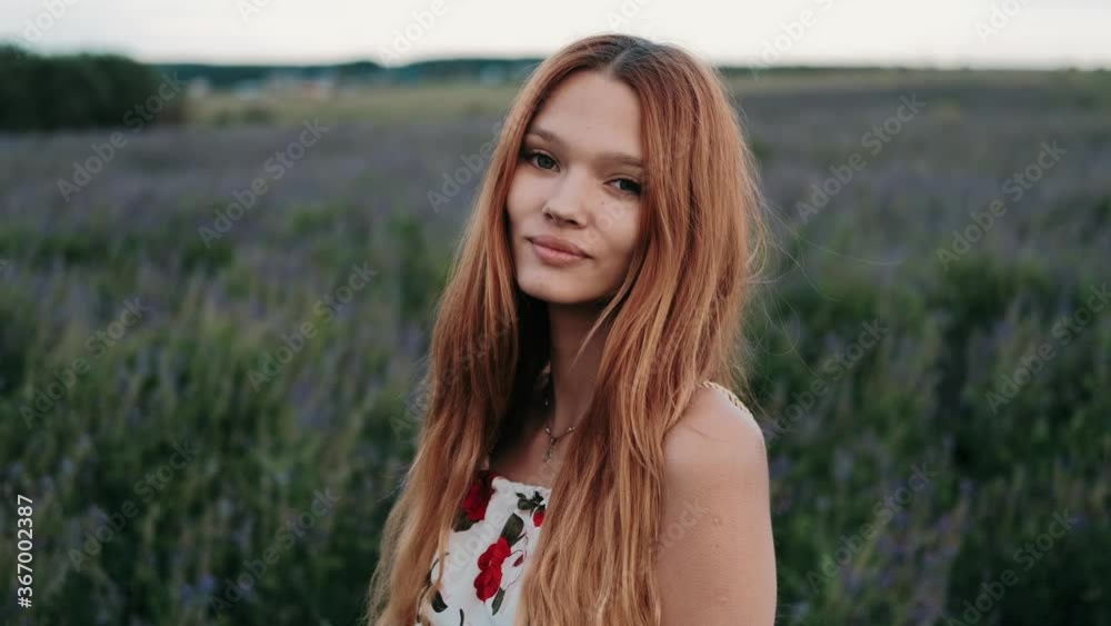 A young redhead girl walking through flowers on flower field. Beautiful carefree girl enjoying nature and sunlight in wheat field at incredible colorful sunset. Freedom concept. A young redhead girl walking through flowers on flower field. Beautiful carefree girl enjoying nature and sunlight in wheat field at incredible colorful sunset. Freedom concept.