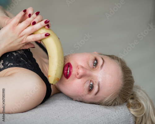 The blonde in black lace underwear erotically eats a banana. Attractive woman with sensual red lips sexually sucks and licks a banana. Oral pleasure.