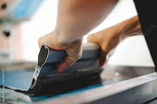 Cropped view of craftsman working on screen printing machine in designer studio 