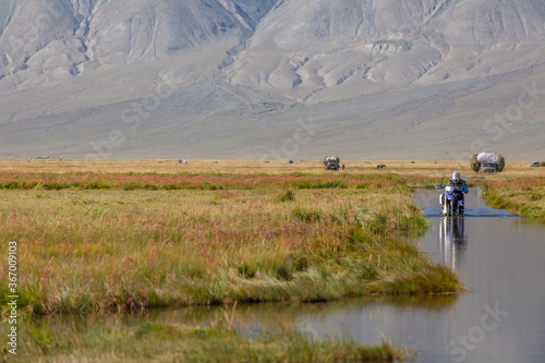 A motorcyclist pushes a motorcycle along a road flooded with water. Altai, Mongolia.