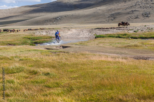 a motorcyclist tries to drive along a road filled with water during a flood after rain. Horses on the back plane