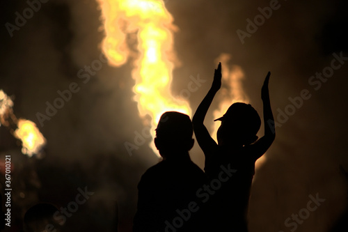 Children in the dark look at the fire from the fire. Silhouettes in the dark on a background of fire