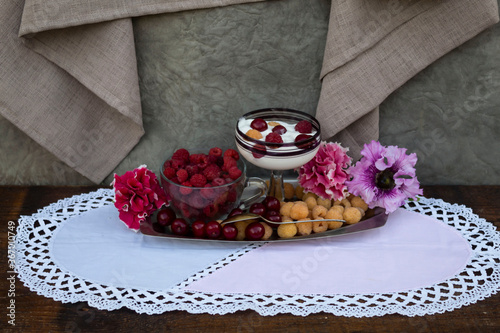 Fototapeta Naklejka Na Ścianę i Meble -  On a metal tray are yellow raspberries, ripe cherries and petunia flowers. There is a red raspberry in a transparent cup. There is ice cream with berries in the bowl..