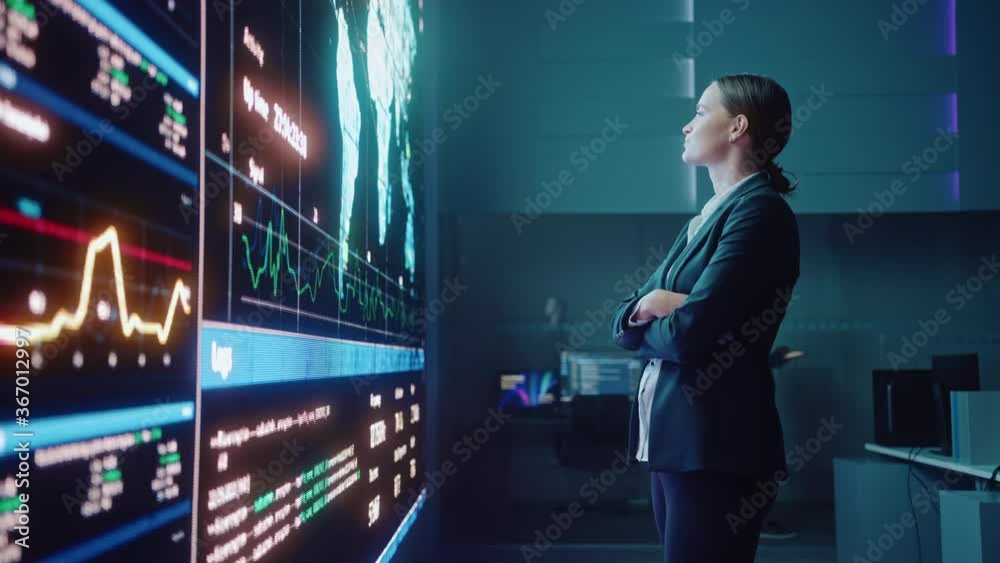 Young Female Computer Science Engineer Looking at Big Screen Display Showing Global Map with Data Points. Telecommunications Technology Company System Control and Monitoring Room with Servers.