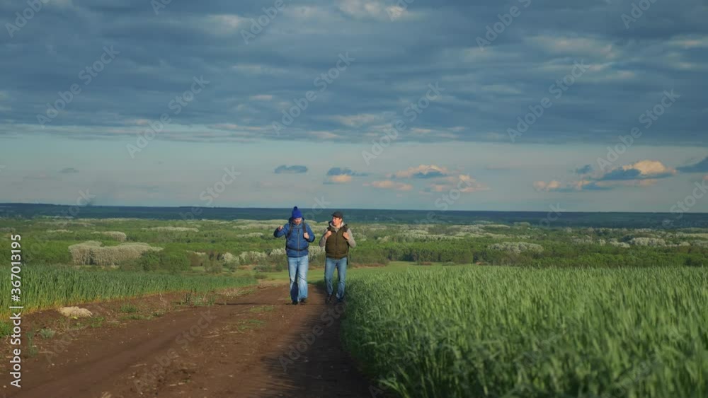 teamwork travel. two man hikers with backpacks walk along a trail next to a field with green grass in nature lifestyle. concept adventure travel hiking healthy. two tourists walk walking talking teamwork travel. two man hikers with backpacks walk along a trail next to a field with green grass in nature lifestyle. concept adventure travel hiking healthy. two tourists walk walking talking