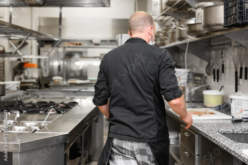 Chef in uniform cooking in a commercial kitchen. Male cook wearing apron standing by kitchen counter preparing food. High quality photo