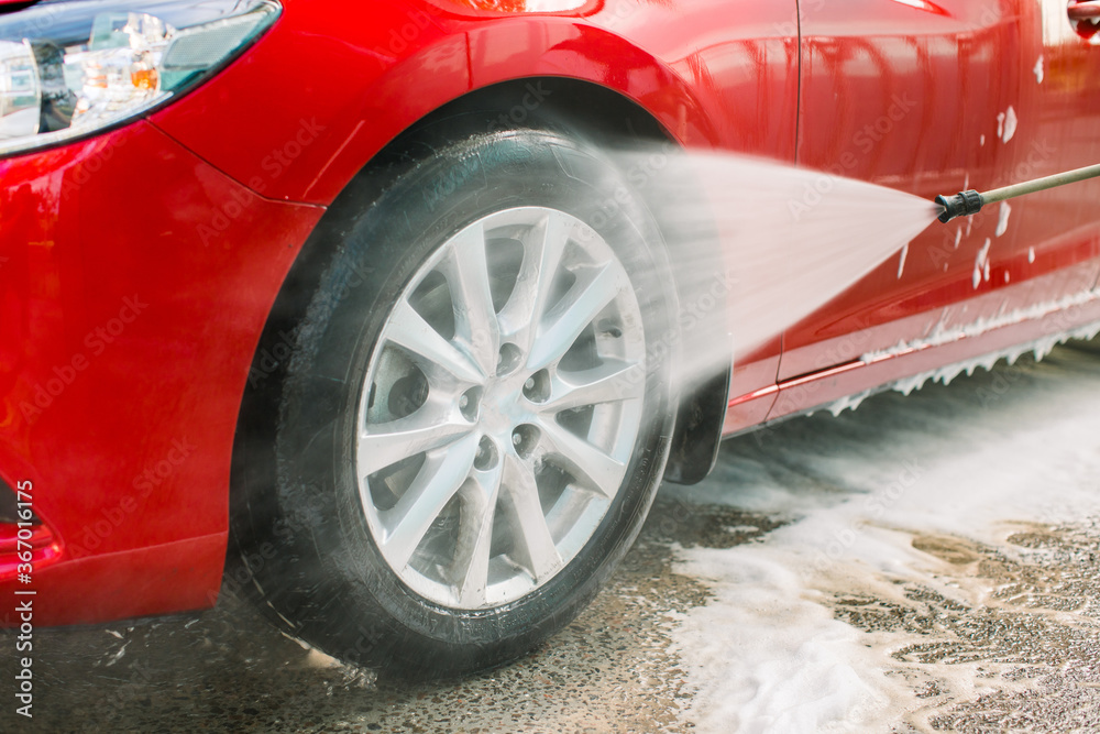 Car washing outdoors. Car washing with soap and high pressure water. Wheel alloy cleaning at car wash station with foam and high pressure water jet. Washing rims.