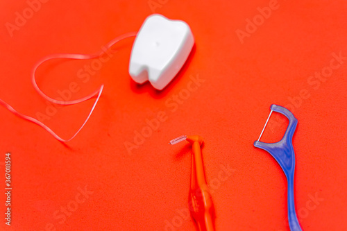 Different types of dental floss and tooth picks on red background. Dental floss in tooth toy shape.