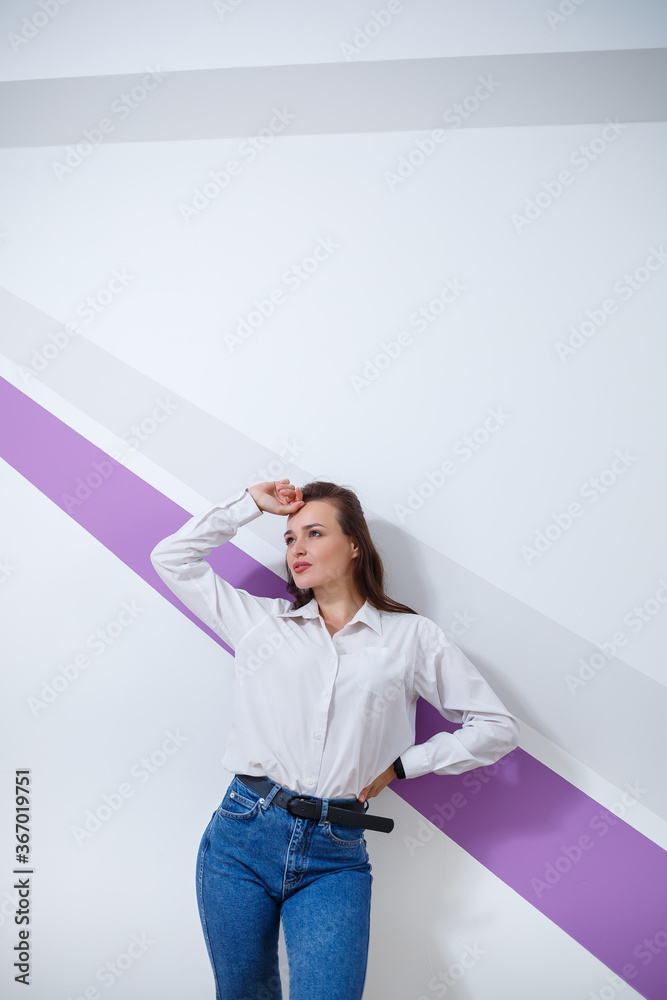 beautiful young white-skinned girl dressed in a white shirt and blue jeans on a light background with a purple stripe beautiful young white-skinned girl dressed in a white shirt and blue jeans on a light background with a purple stripe