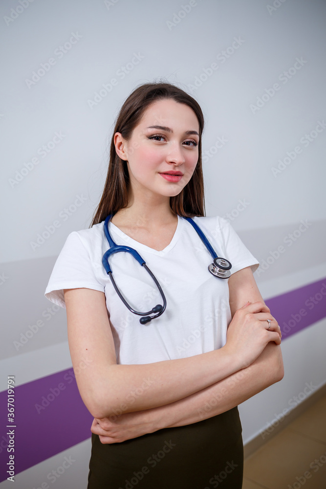 A girl of European appearance with a phonendoscope on her neck. Attractive young brunette woman smiles. She is a young doctor, intern student A girl of European appearance with a phonendoscope on her neck. Attractive young brunette woman smiles. She is a young doctor, intern student