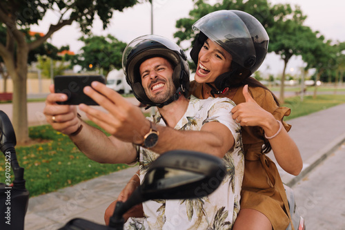 Cheerful Stylish Couple Satting On Modern Motorbike Outdoors and making a selfie with a smartphone