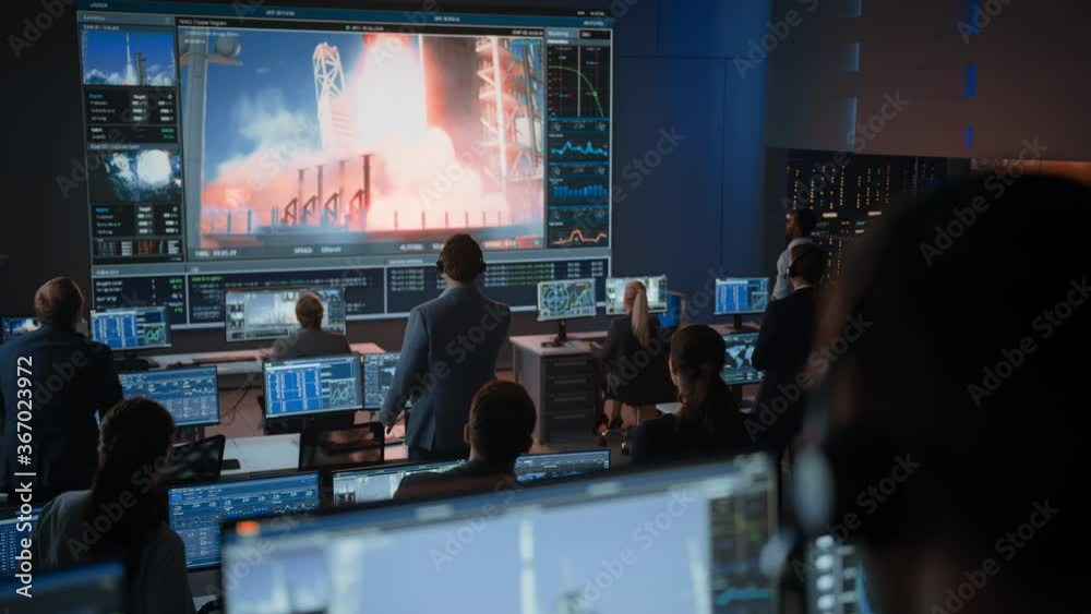 Group of People in Mission Control Center Witness Successful Space Rocket Launch. Flight Control Employees Sit in Front Computer Displays and Monitor the Crewed Mission. Team Stand Up and Clap Hands. Group of People in Mission Control Center Witness Successful Space Rocket Launch. Flight Control Employees Sit in Front Computer Displays and Monitor the Crewed Mission. Team Stand Up and Clap Hands.