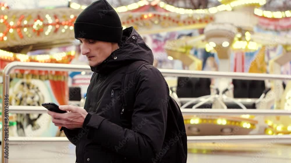 Handsome young man using smartphone in the city, amusement park at the evening
