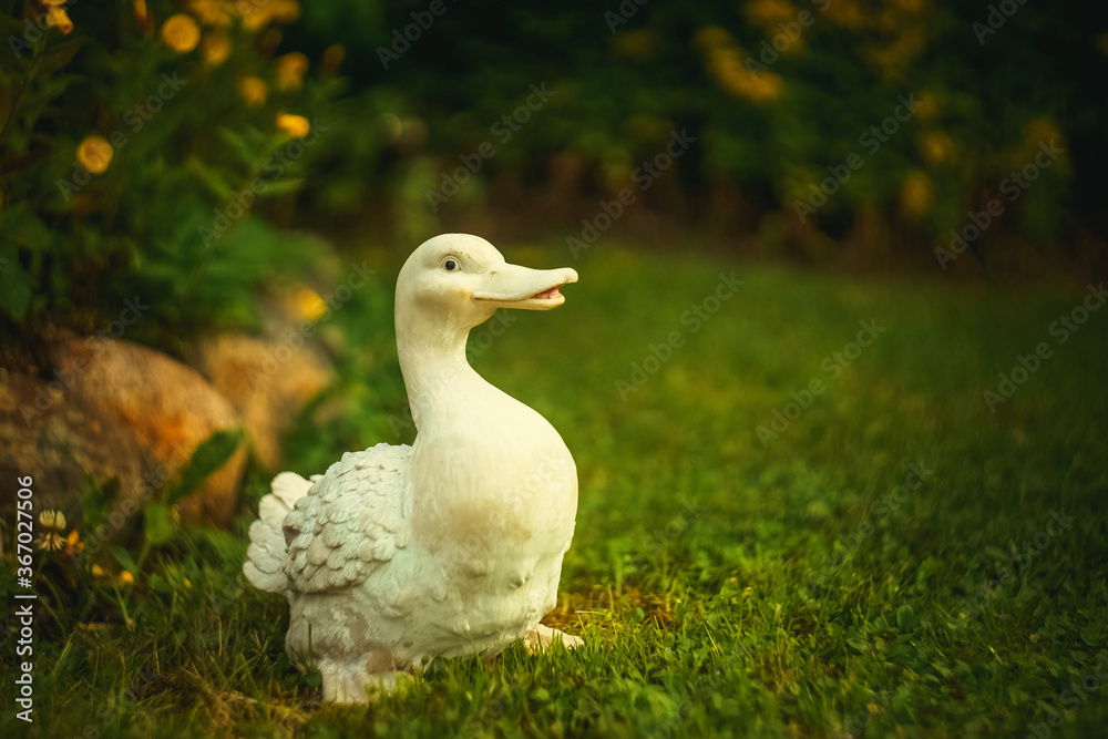 White decorative duck in the garden on the green grass next to a flowerbed of stones White decorative duck in the garden on the green grass next to a flowerbed of stones