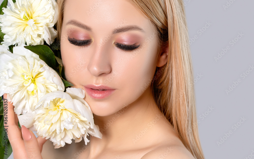 Portrait of a beautiful blonde woman with long hair, beautiful fresh makeup and healthy clean skin with peonies in her hands. Makeup and cosmetology concept. Portrait of a beautiful blonde woman with long hair, beautiful fresh makeup and healthy clean skin with peonies in her hands. Makeup and cosmetology concept.