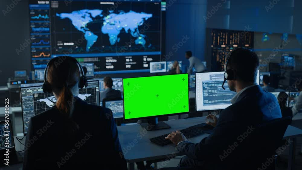 Green Screen Horizontal Mock Up on Computer Display Used by Controller in Surveillance Control Center with Global Map Tracking on a Big Digital Screen. Monitoring Room Employees Analyze Big Data. Green Screen Horizontal Mock Up on Computer Display Used by Controller in Surveillance Control Center with Global Map Tracking on a Big Digital Screen. Monitoring Room Employees Analyze Big Data.