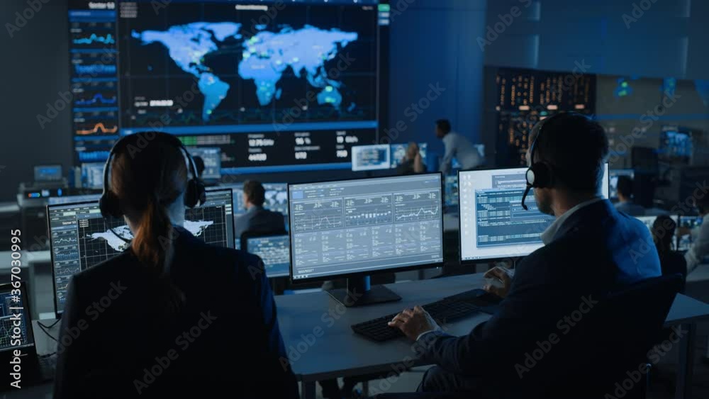 Software Engineers Working in a Modern Monitoring Office with Live Ananlysis Feed from a Global Map on a Big Digital Screen. Monitoring Room Big Data Scientists and Managers Sit in Front of Computers. Software Engineers Working in a Modern Monitoring Office with Live Ananlysis Feed from a Global Map on a Big Digital Screen. Monitoring Room Big Data Scientists and Managers Sit in Front of Computers.