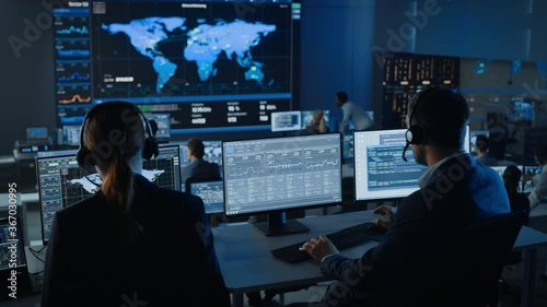 Software Engineers Working in a Modern Monitoring Office with Live Ananlysis Feed from a Global Map on a Big Digital Screen. Monitoring Room Big Data Scientists and Managers Sit in Front of Computers. photo