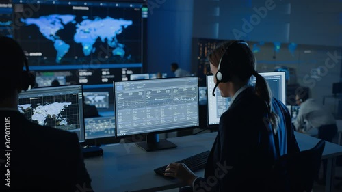 Female Specialist Works on a Computer with Live Ananlysis Feed from a Global Map on a Big Digital Screen. Employees Sit in Front of Displays with Financial Stock Market Trading Info and Big Data. photo