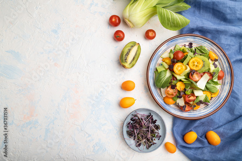 Vegetarian salad of pac choi cabbage, kiwi, tomatoes, kumquat, microgreen sprouts on a white concrete background. Top view, copy space.