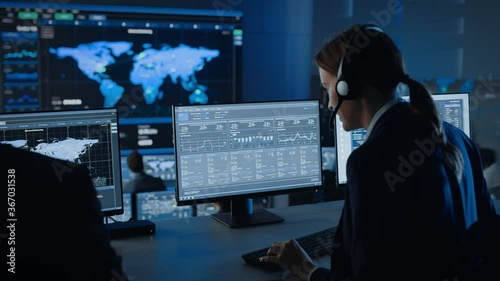 Female Specialist Works on a Computer with Live Ananlysis Feed from a Global Map on a Big Digital Screen. Employees Sit in Front of Displays with Financial Stock Market Trading Info and Big Data. photo