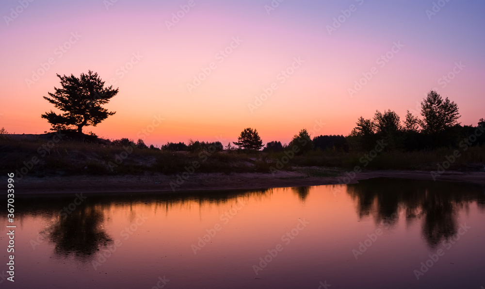 quiet smal lake at the twilight, forest silhouette on a pink sky