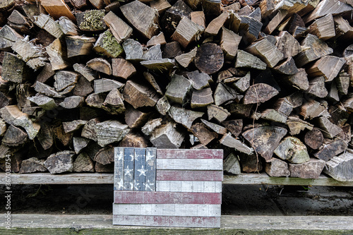 Photograph of stacked, split, aged firewood with a wooden American Flag in front of it photo