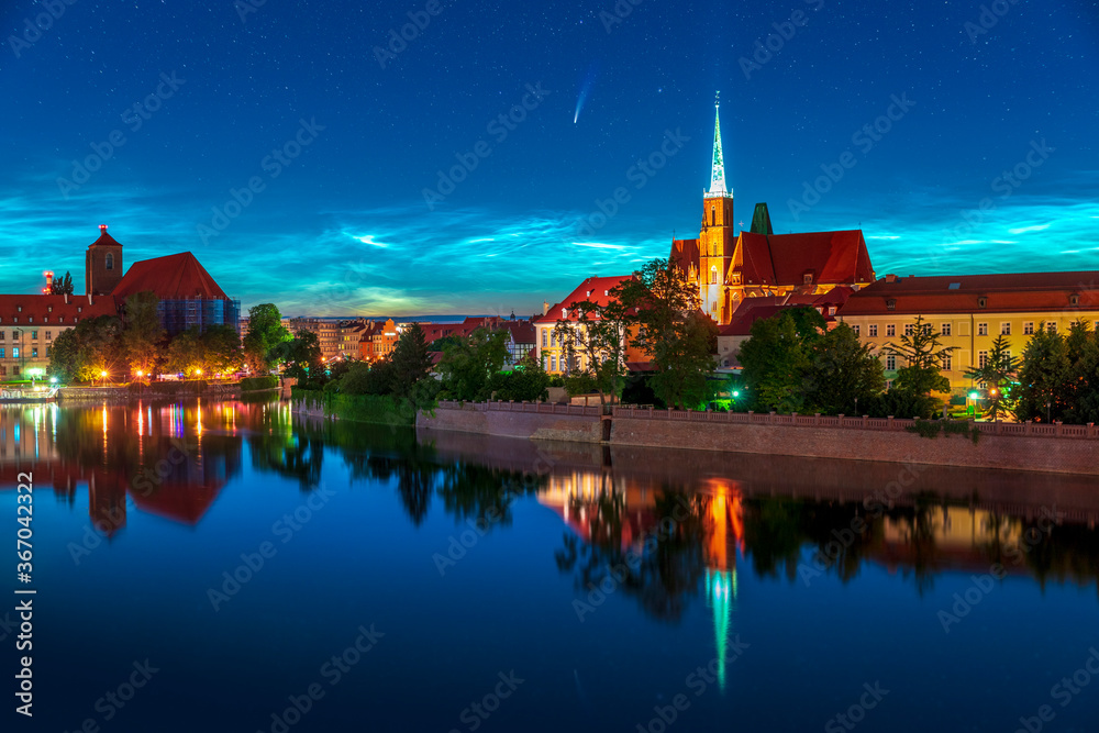 Long period comet NEOWISE and noctilucent clouds (NLC) seen above Wroclaw in Poland. Beautiful night shining clouds with rare astro phenomen over the cityline. The sky reflects on the Oder river