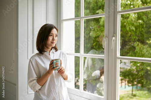 Tableau sur toile young asian woman looking out of window at home