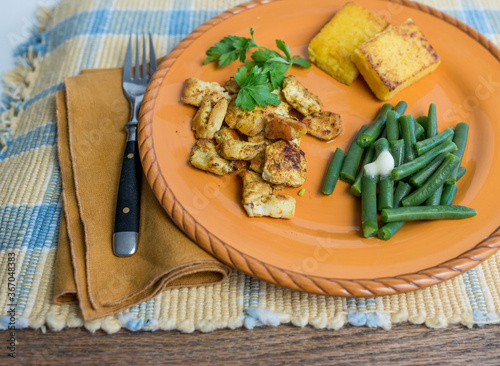 Colorful orange ceramic plate with spiced chicken cubes and funchi (polenta or corn meal mush), a traditional food item in Aruba.  photo