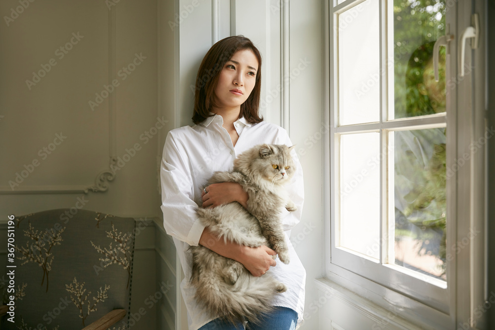 young asian woman standying by window at home holding a cat young asian woman standying by window at home holding a cat
