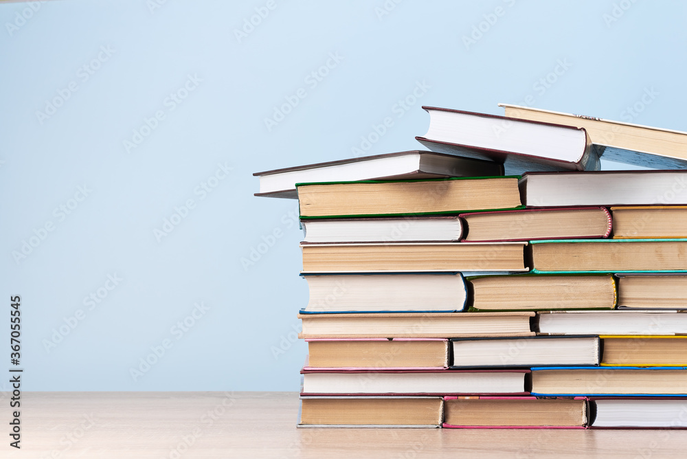 A large stack of books stands on a wooden table against a light blue wall, space for text A large stack of books stands on a wooden table against a light blue wall, space for text
