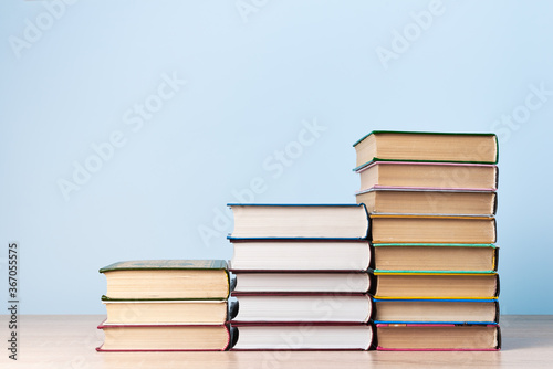 Three stacks of books of different heights, standing on a wooden table against a light blue wall, space for text
