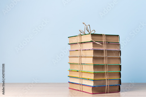 A stack of books tied with a rope stands on a wooden table against a light blue wall, a place for text