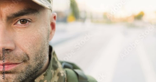 Portrait of Caucasian handsome young man soldier in cap with backpack looking confident at street. Close up of half face of male militarian with wise brave face outdoor at bus stop. Military uniform. photo