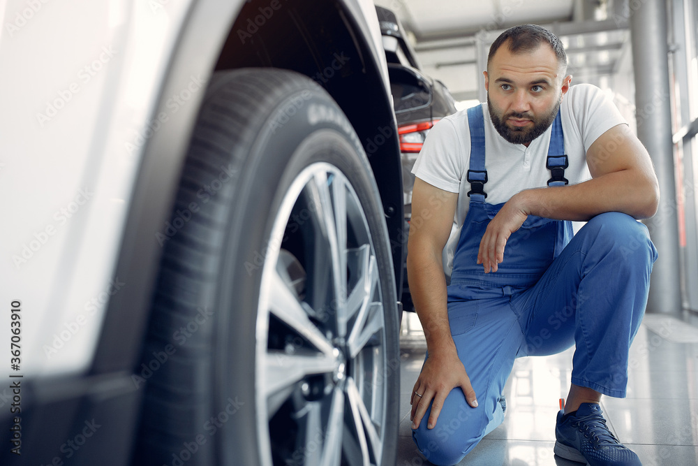 Wrker in a car salon. Expert checks the car. Man in a blue uniform.