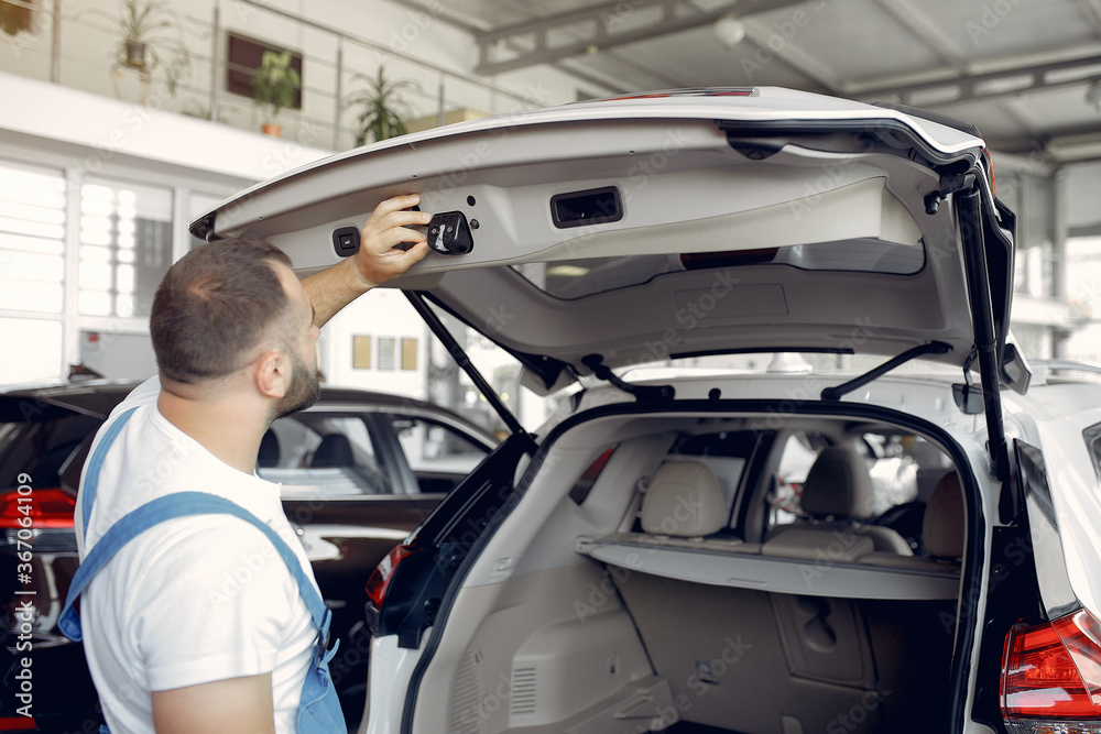 Wrker in a car salon. Expert checks the car. Man in a blue uniform. Wrker in a car salon. Expert checks the car. Man in a blue uniform.