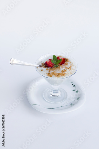 Traditional Turkish Rice Puding in stylish glass bowl wwith spoon on white background.