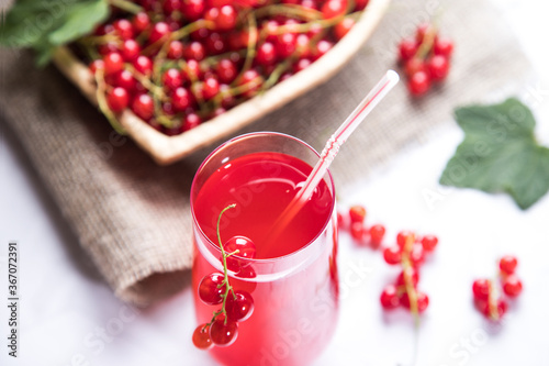 Sprigs of red currant berries are lying in a wicker plate, a Morse of berries is in a glass glass on a light background