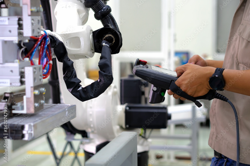 Smart factort concept: An engineer use handheld controller setting industrial robot in productionplant.