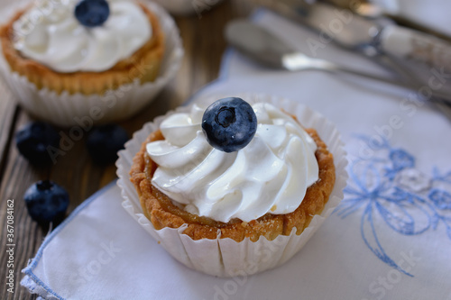 One shortcrust tartlet with whipped egg white cream on top, garnished with blueberries on a napkin next to others photo